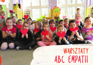 Zdjęcie grupy fioletowej dzieci siedzą na dywanie trzymają serca w ręku pod nimi napis Warsztaty ABC Empatii